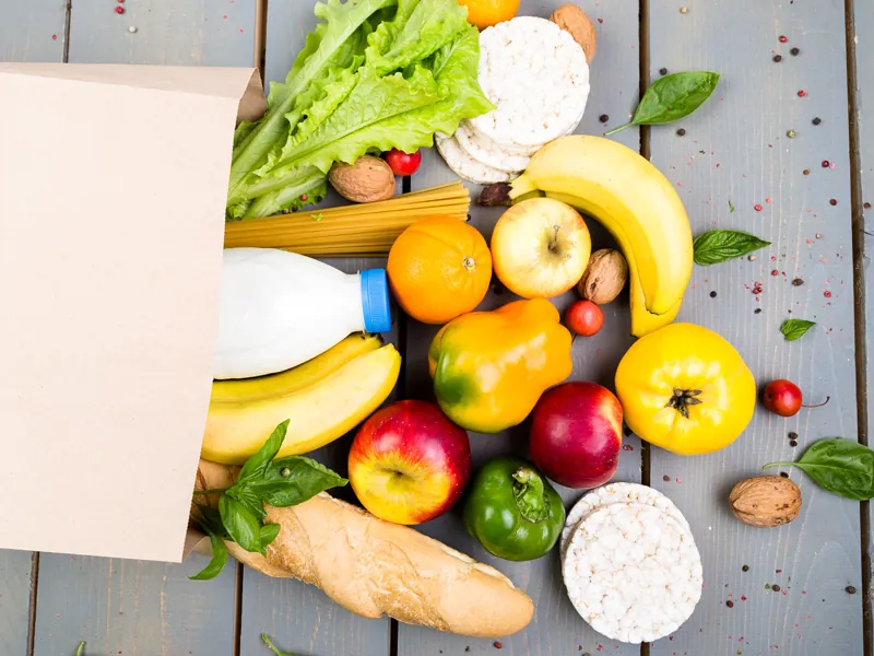 Fresh fruit, vegetables, bread and milk spilling from a paper grocery bag