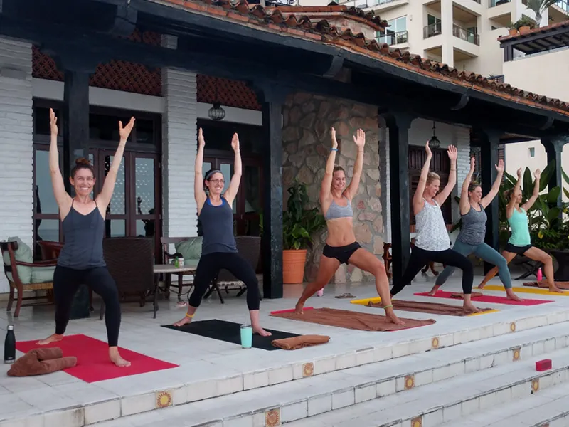 Group holding warrior pose on red mats on a villa terrace