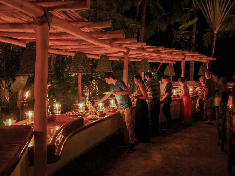 Long dinner tables under a thatched palapa glowing with candlelight