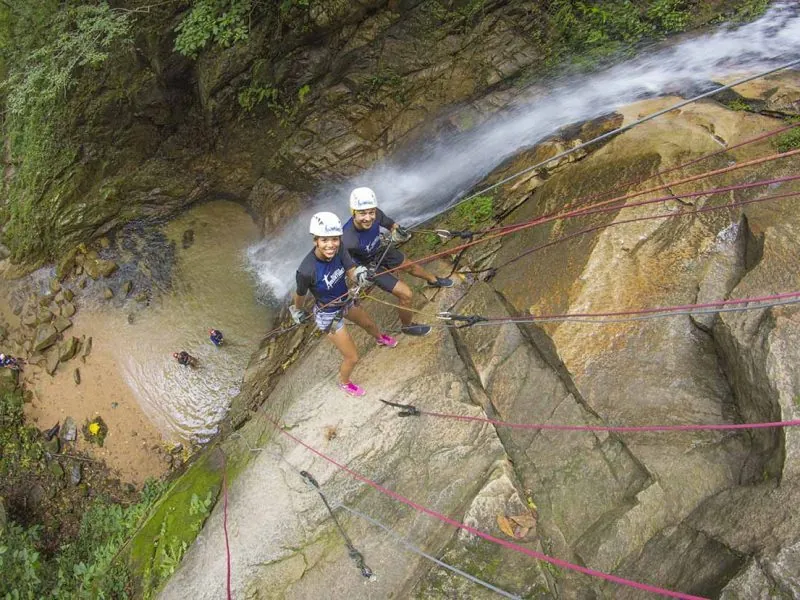 Two guests rappelling beside a waterfall