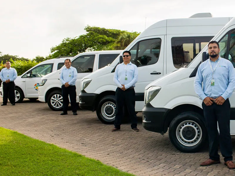 Uniformed drivers standing beside white vans and a Sprinter at the fleet lot in Puerto Vallarta